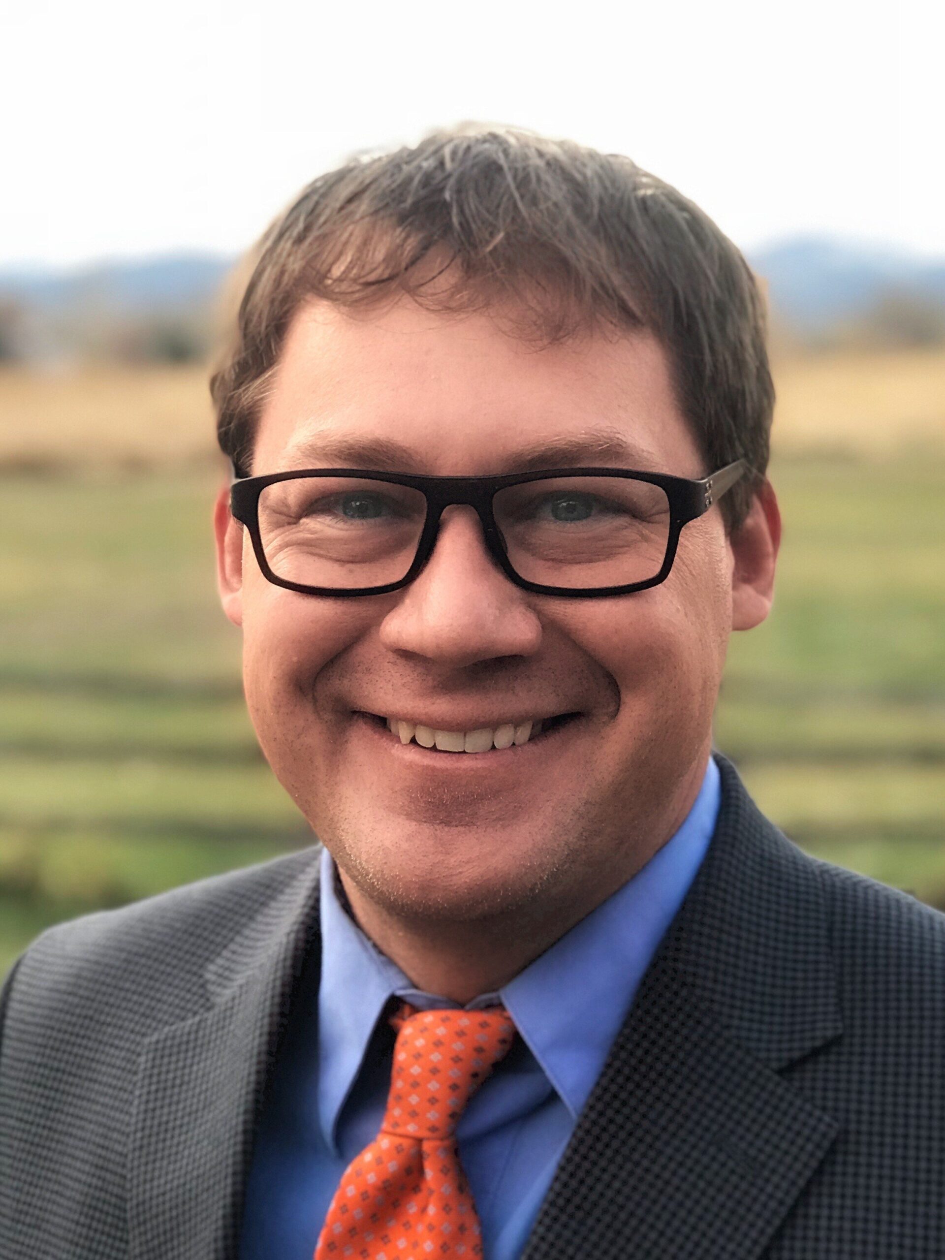 Professional headshot of man wearing glasses and suit outdoors