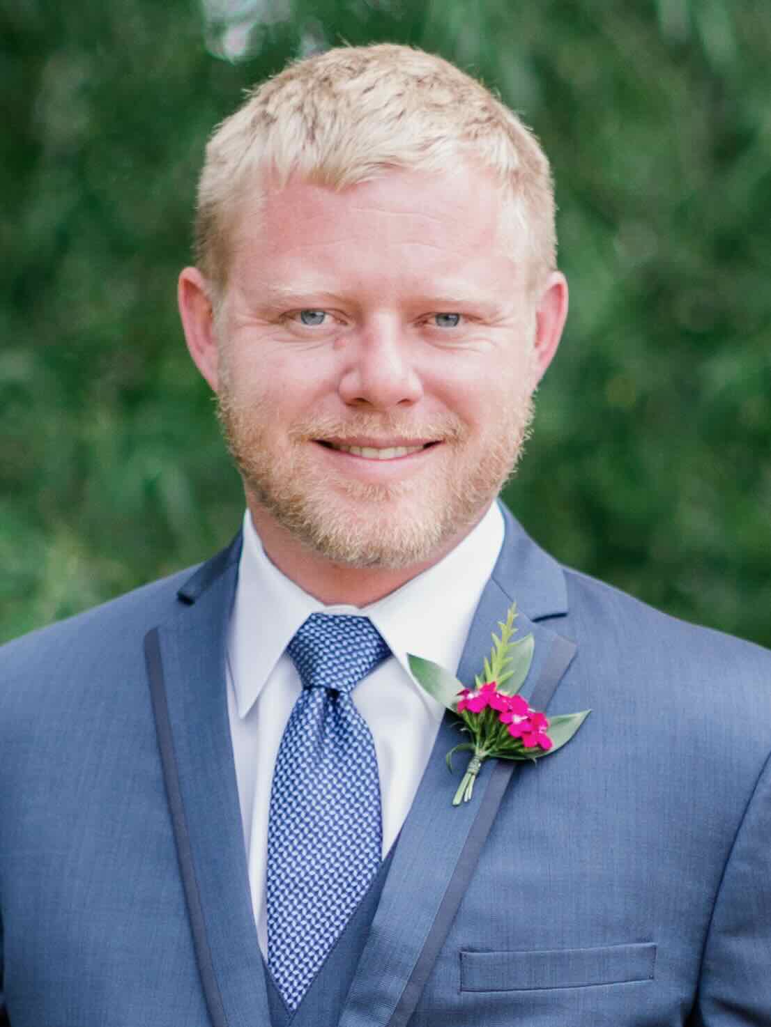 Professional headshot of blond man in blue suit and red tie