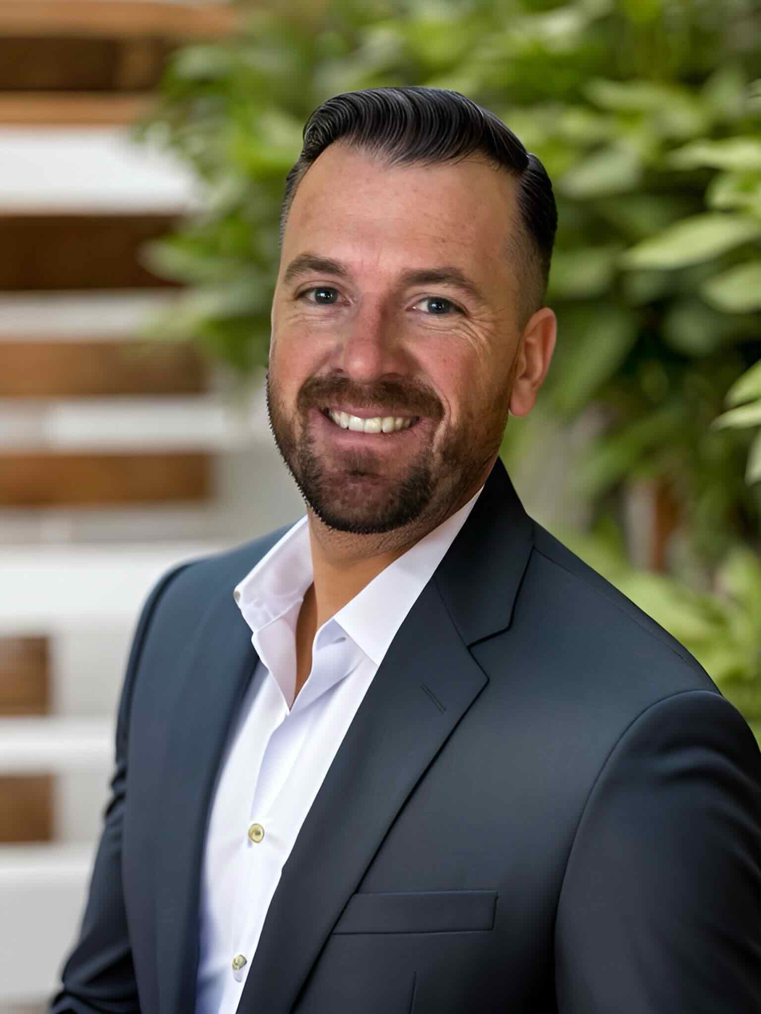 Professional headshot of man in gray suit smiling outdoors