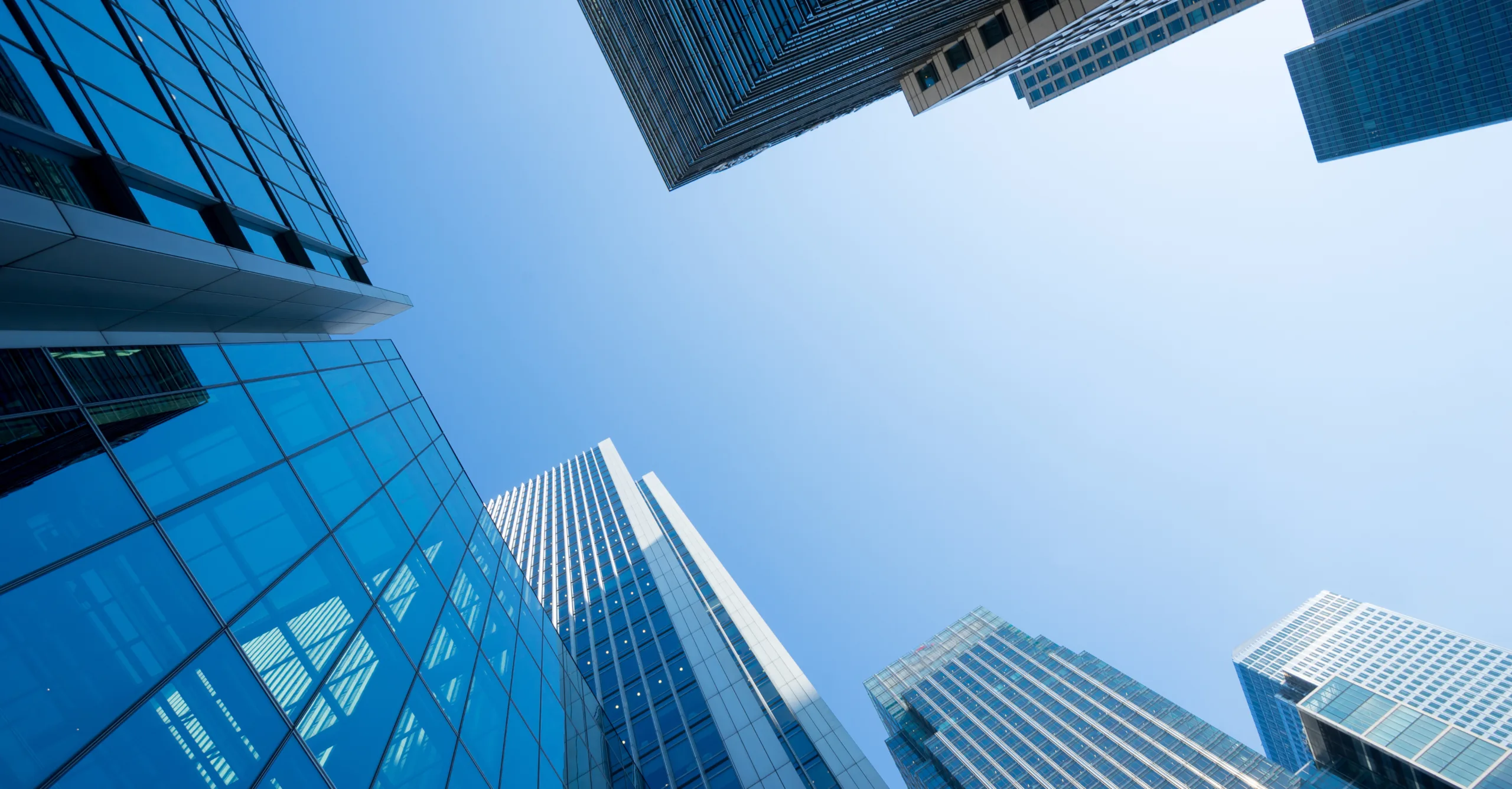 Looking up at glass skyscrapers converging toward the center under a clear blue sky, from ground level